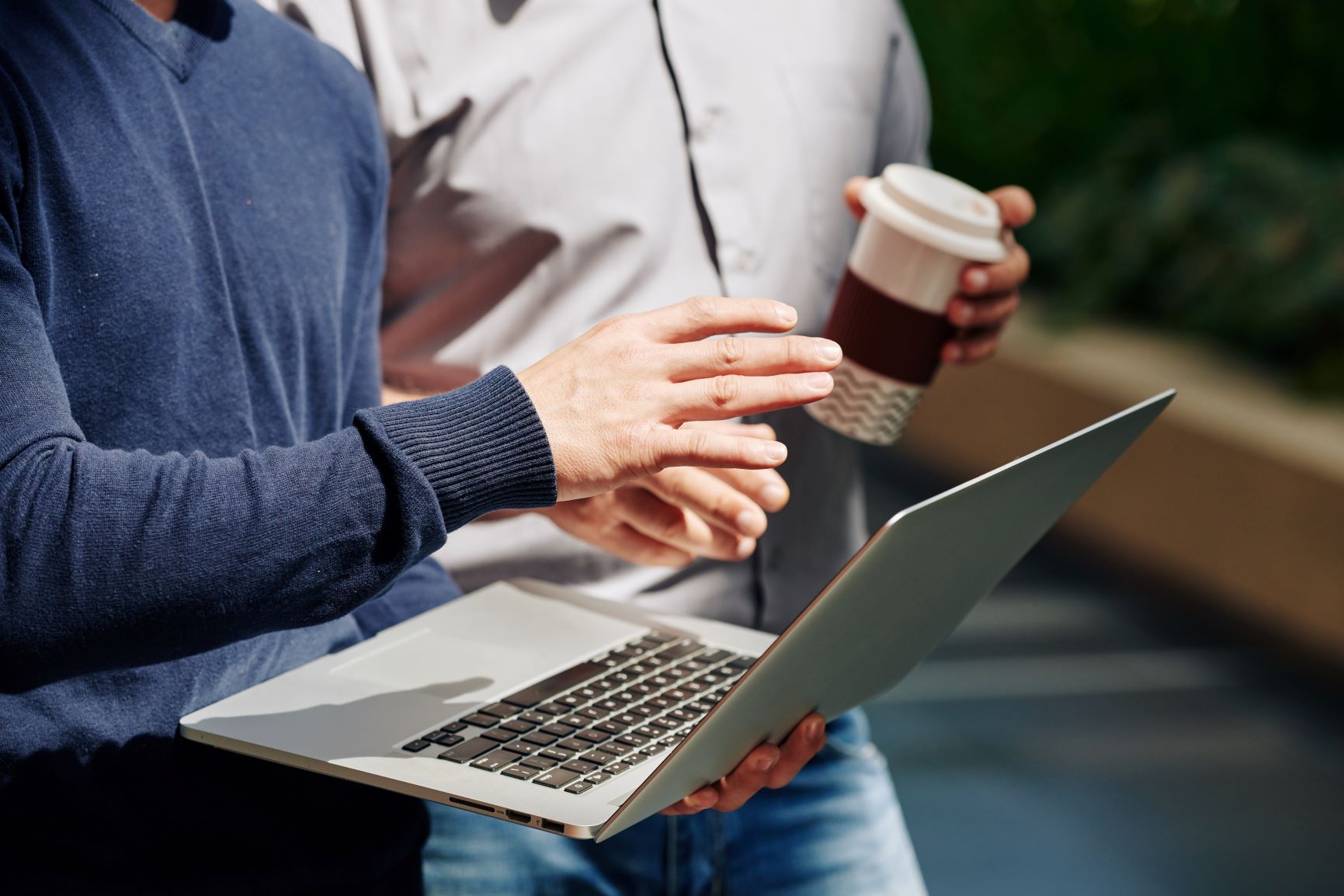 businessman holding a laptop discussing with another man the need for Outsourced HR Generalist services from Optima Office